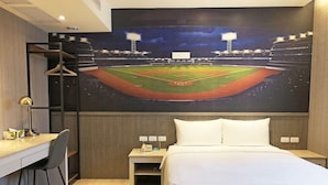 A hotel room with a bed, a desk, and a chair. There is a painting of a baseball field on the wall. - Kindness Hotel Lio He Ye Shi (Kaohsiung)