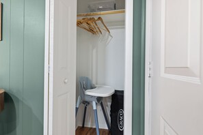 A room with a white door, a grey chair, a white table, and a black bag with the brand 'GRACO' on it. - Cottage Nest at Downtown Berkeley Springs (Berkeley Springs)