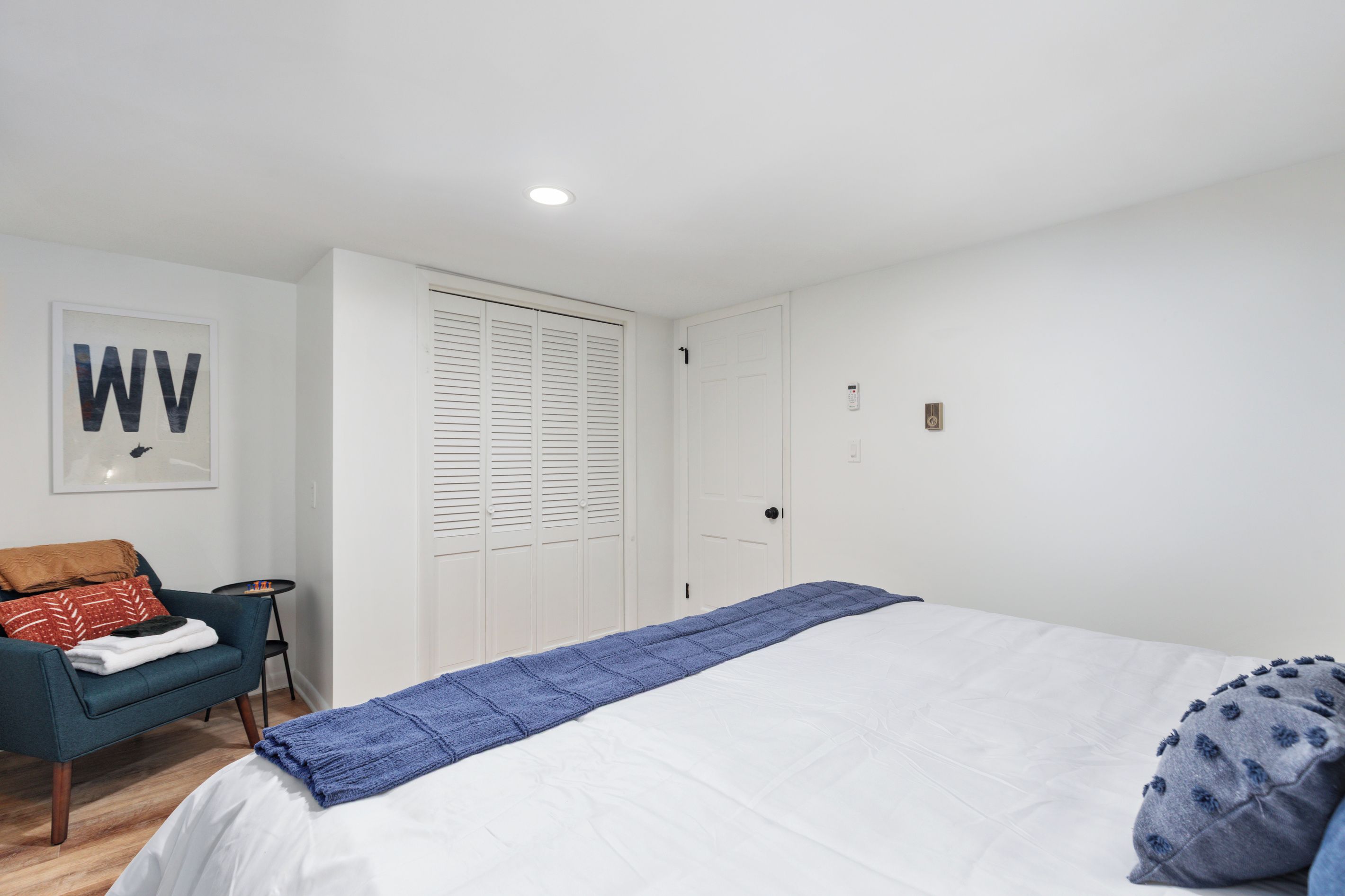 Ein Schlafzimmer mit einem Bett, einem Sessel, einem kleinen Tisch, einem Kleiderschrank und einer Tür.