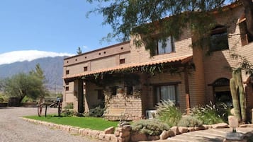 Um edifício de dois andares em tijolo com um pátio, um cacto e montanhas ao fundo.