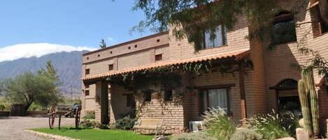 A two-story brick building with a patio area, a cactus, and a mountain backdrop.