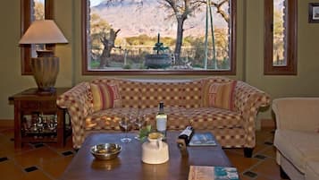Uma sala de estar acolhedora com um sofá xadrez, uma mesa de centro com um livro, um abajur e vista para uma paisagem montanhosa através de uma grande janela.