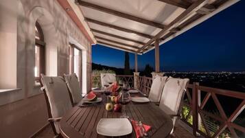 An outdoor dining area with a table set for two, overlooking a cityscape at dusk.
