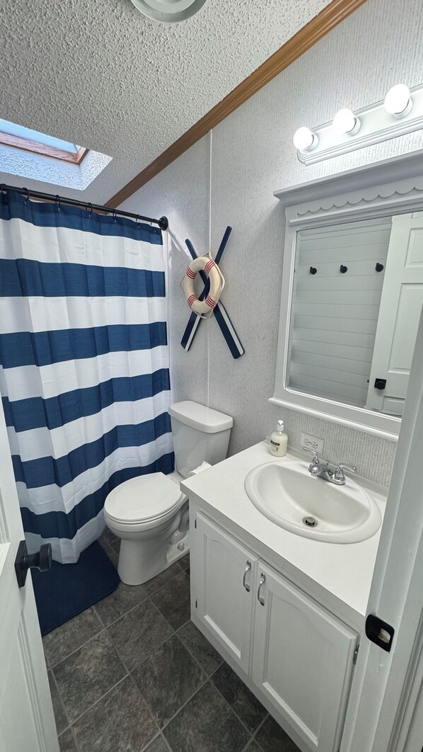 Een badkamer met een gestreepte douchegordijn, toilet, wastafel met spiegel erboven en een handdoekrek.