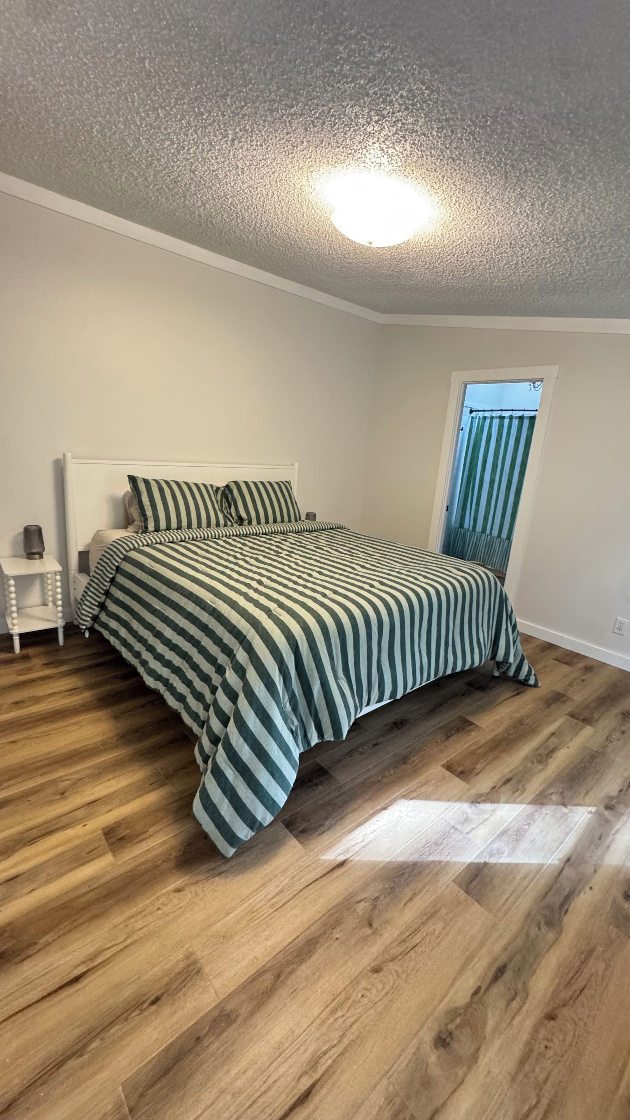 A bedroom with a bed, a nightstand, a window with curtains, and a wooden floor.