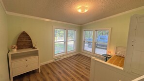 A bedroom with a wooden floor, a built-in shelf, a bed with a headboard, and a window with blinds.