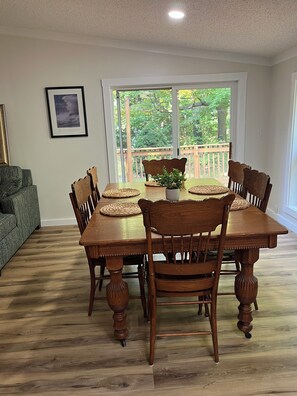 Ein Esszimmer mit Holztisch und Stühlen, einer Topfpflanze und Blick auf einen Balkon mit Grünpflanzen.