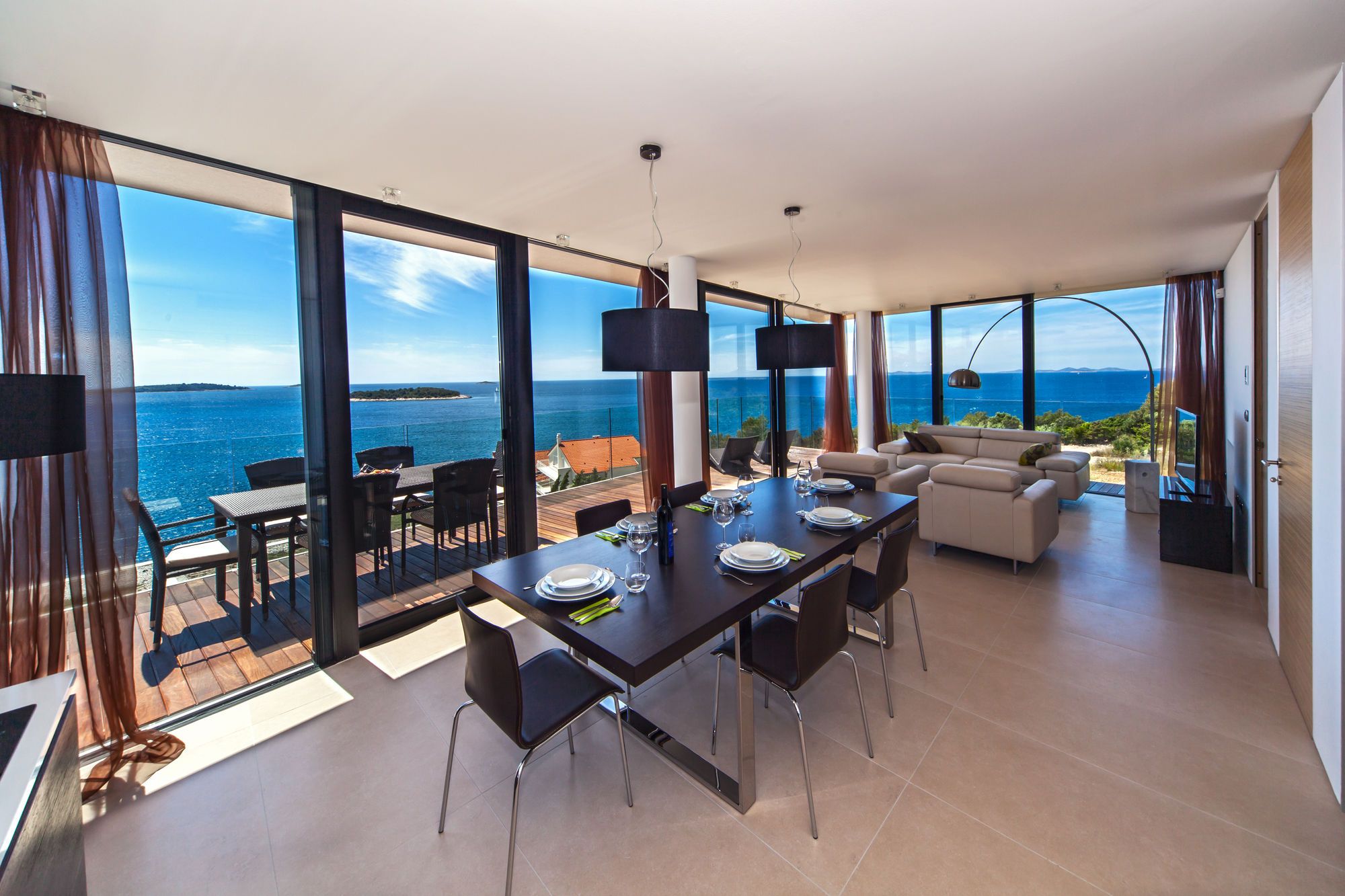 A modern dining area with a view of the sea, a sofa, and a television.