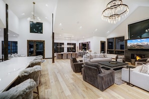 A modern living room with a fireplace, a dining area with a long table, and a large TV screen. - NEW Trailblazer Lodge, the Ultimate Family Destination (Breckenridge)
