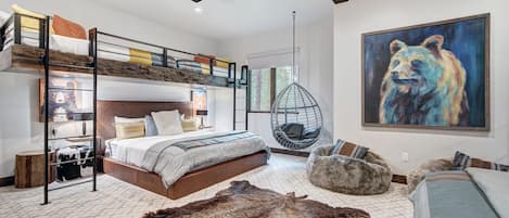A modern bedroom with bunk beds, a hanging chair, a rug, and a bear painting.