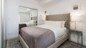 A hotel room with a large bed, a bedside table with a lamp, a mirror, and a small picture on the wall. - Skyline Suite Near CN Tower Downtown (Toronto)