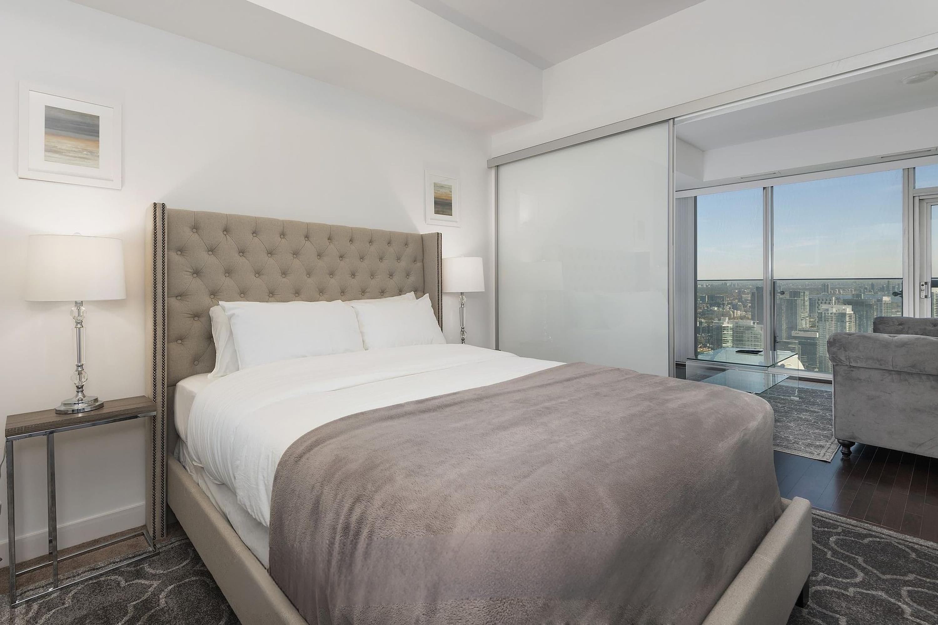 A modern hotel room with a large bed, a glass partition, and a city view.