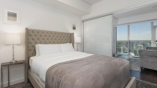 A modern hotel room with a large bed, a glass partition, and a city view. - Skyline Suite Near CN Tower Downtown (Toronto)