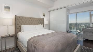 A modern hotel room with a large bed, a glass partition, and a city view.