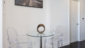 A modern room with a glass table and two clear chairs, a framed picture on the wall, and a door in the background. - Skyline Suite Near CN Tower Downtown (Toronto)