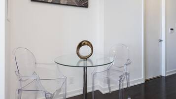 A modern room with a glass table and two clear chairs, a framed picture on the wall, and a door in the background.