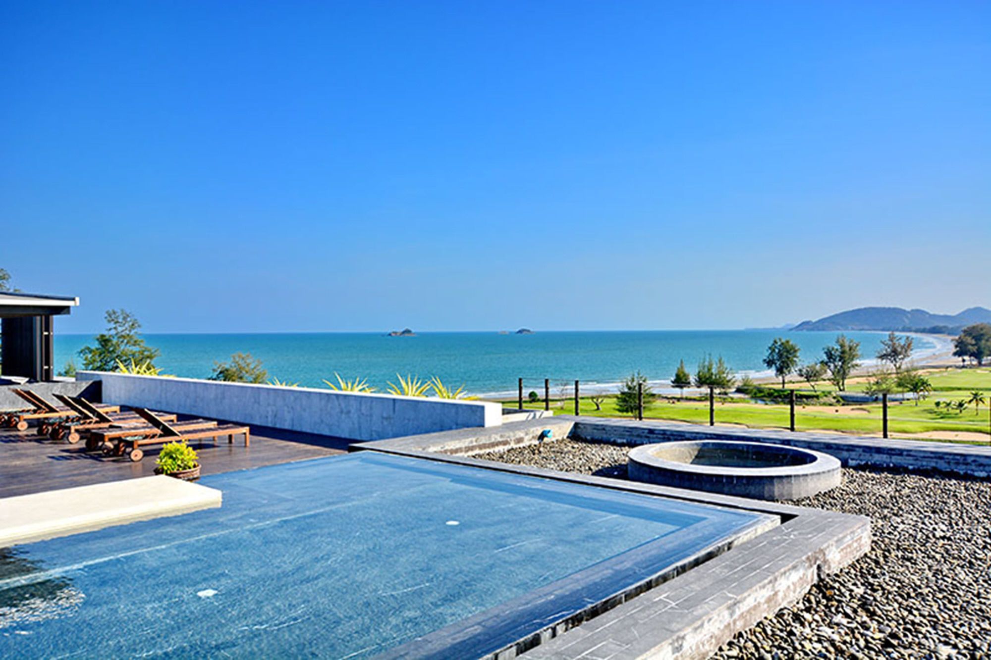 A rooftop infinity pool with a view of the sea and a landscaped area with seating.