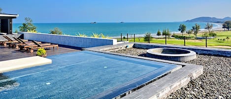A rooftop infinity pool with a view of the sea and a landscaped area with seating.
