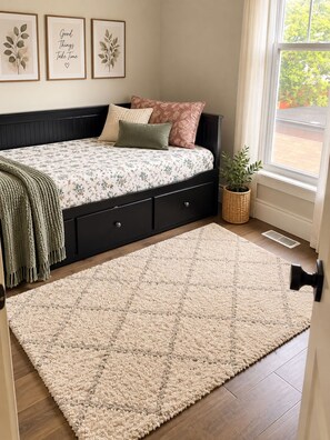 A bedroom with a bed, a large beige rug, a window with a view, and three framed pictures on the wall. -     Cottage Charm Meets Modern Comfort in the Heart of Woodstock (Woodstock)
