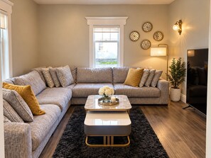 A living room with a sectional sofa, a coffee table, a black rug, decorative wall lights, and a potted plant. -     Cottage Charm Meets Modern Comfort in the Heart of Woodstock (Woodstock)