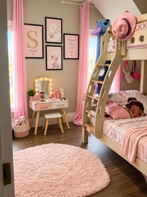 Ein Kinderzimmer mit Etagenbett, Schminktisch mit Spiegel und gerahmten Bildern an der Wand.