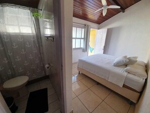A bedroom with a bed, a ceiling fan, and a bathroom with a toilet and shower curtain. - Btuga Guest House (Arraial do Cabo)