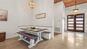 A room with a white wooden wall, a table with a bench, a door with glass panels, and a chandelier. - Broken Bow Cabin w/ Hot Tub, Creek & 3 Acres (Broken Bow)