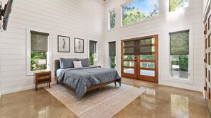 A bedroom with a bed, a nightstand, a window, and a door. - Broken Bow Cabin w/ Hot Tub, Creek & 3 Acres (Broken Bow)