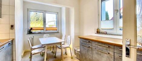 Una cocina con una mesa de comedor y sillas, una ventana con persianas y una puerta con cerradura.