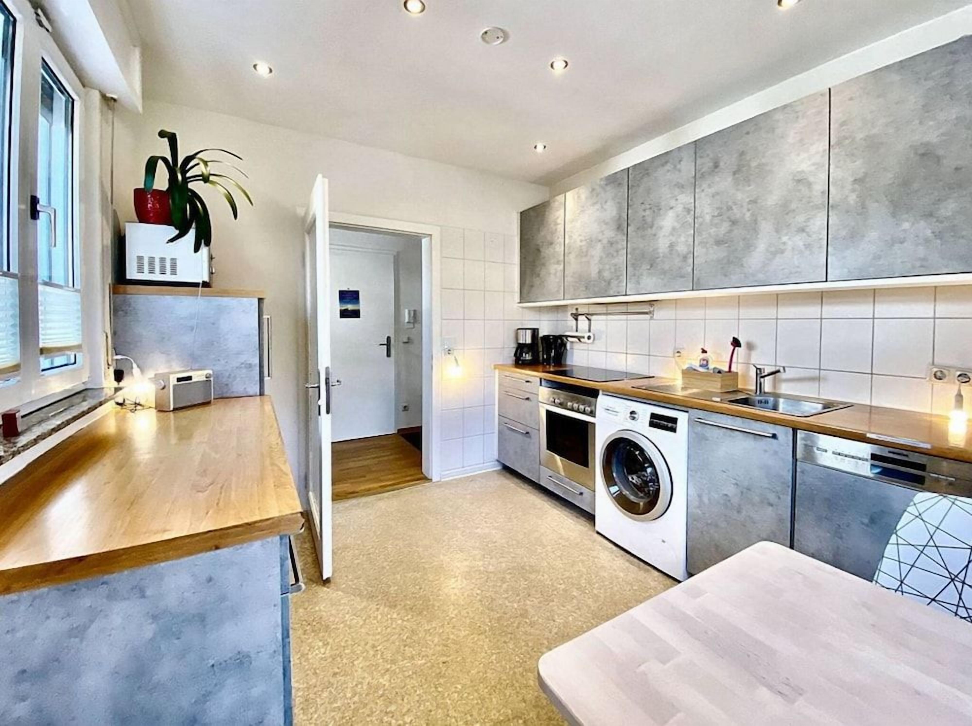 Eine moderne Küche mit integriertem Waschmaschine, einer Holz Arbeitsplatte und Blick auf den angrenzenden Wohnbereich.