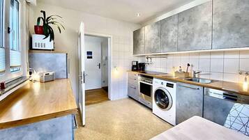 Eine moderne Küche mit integriertem Waschmaschine, einer Holz Arbeitsplatte und Blick auf den angrenzenden Wohnbereich.