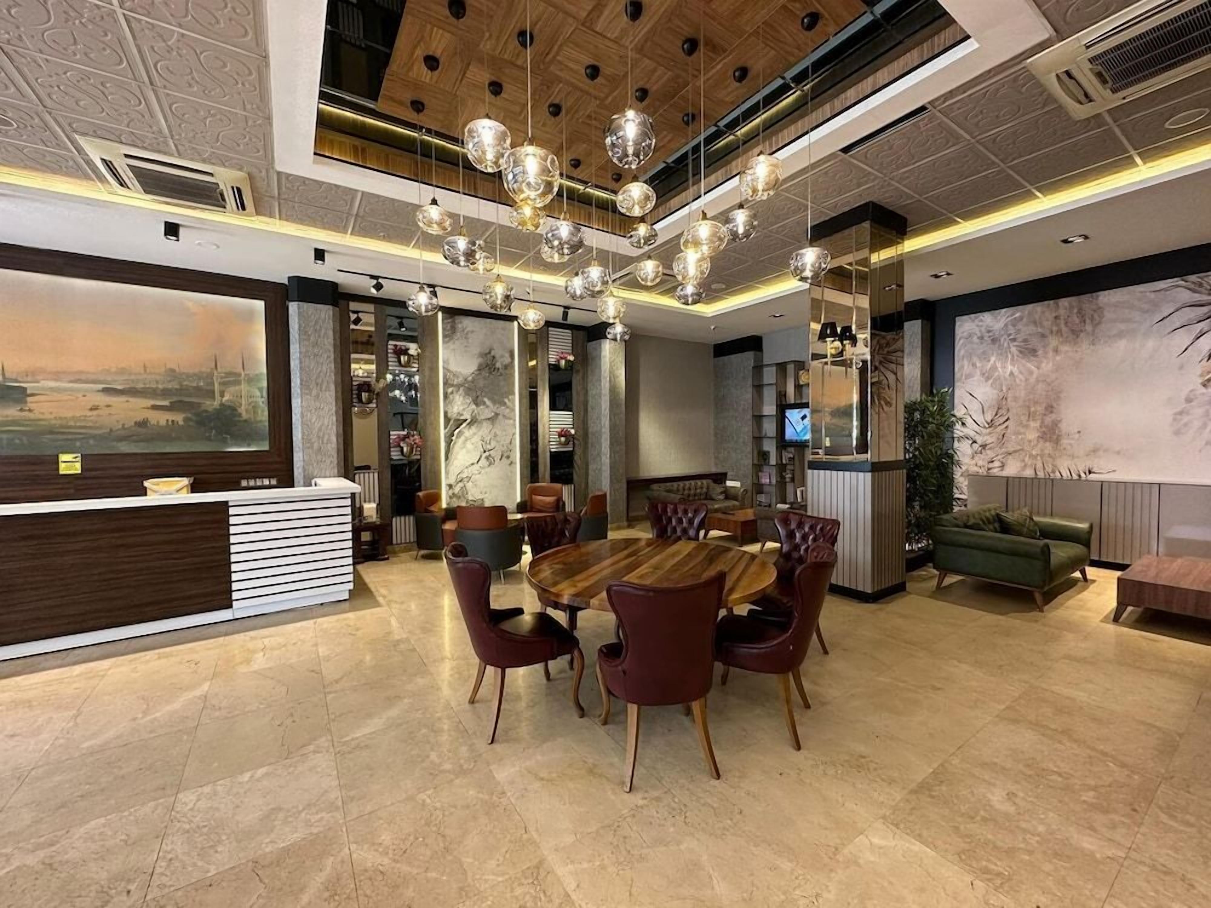 A hotel lobby with a reception desk, a round dining table with chairs, a green sofa, and a large abstract painting on the wall.