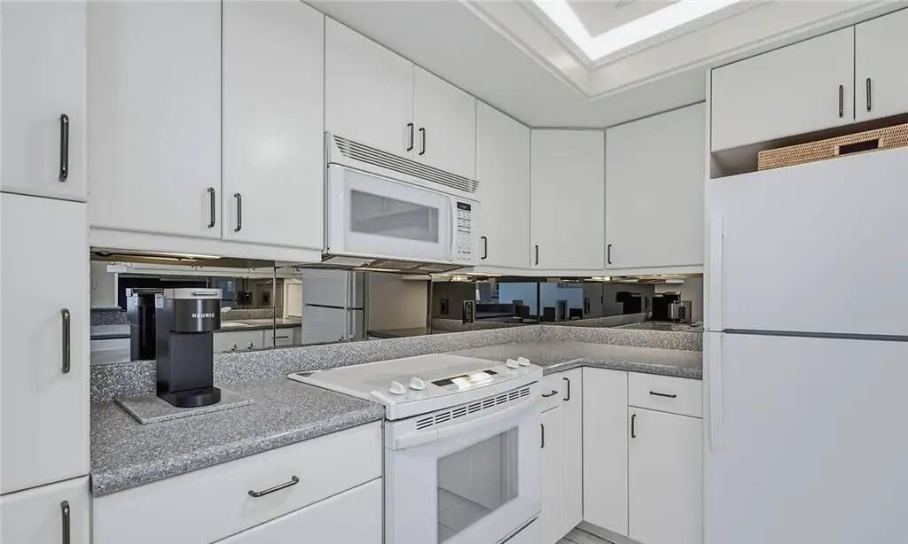 A modern kitchen with white cabinets, a built-in microwave, a coffee machine, and a gas stove.