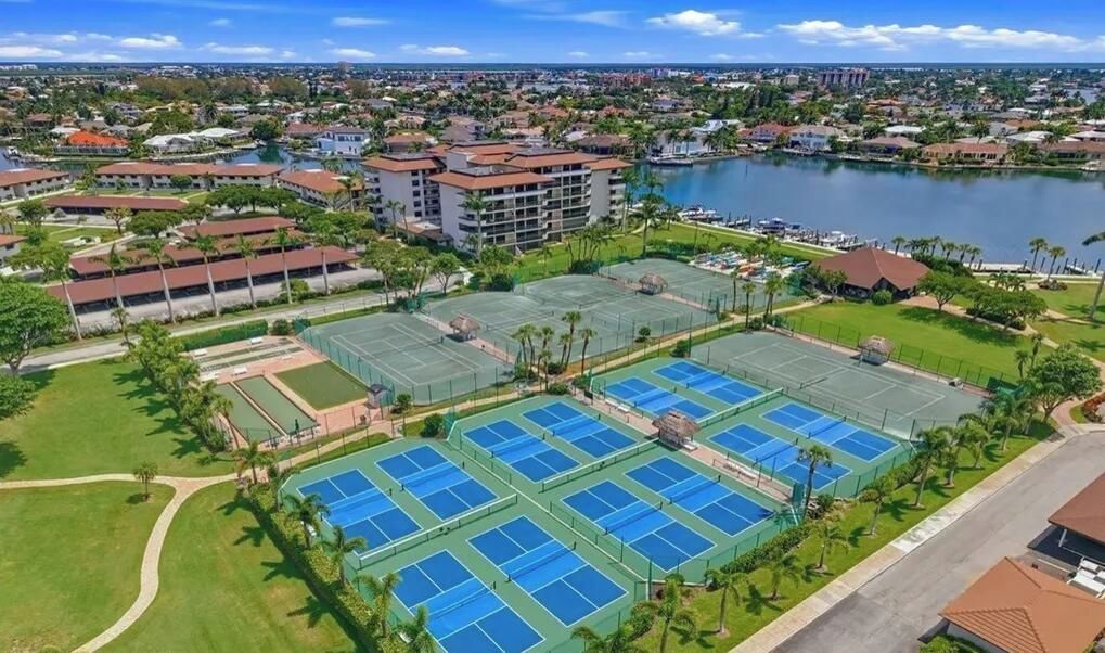 A residential area with multiple tennis courts, a large body of water, and surrounding buildings.
