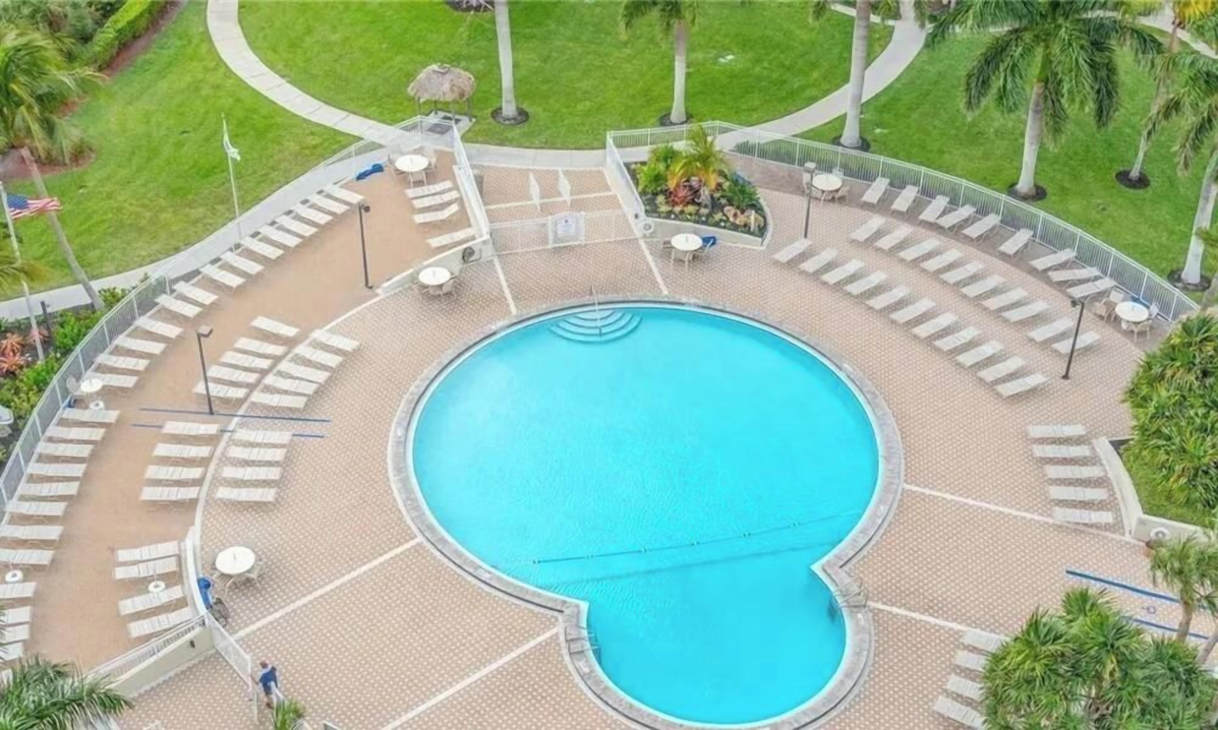Una piscina circular con sillas de descanso y sombrillas, rodeada por una terraza empedrada y palmeras.