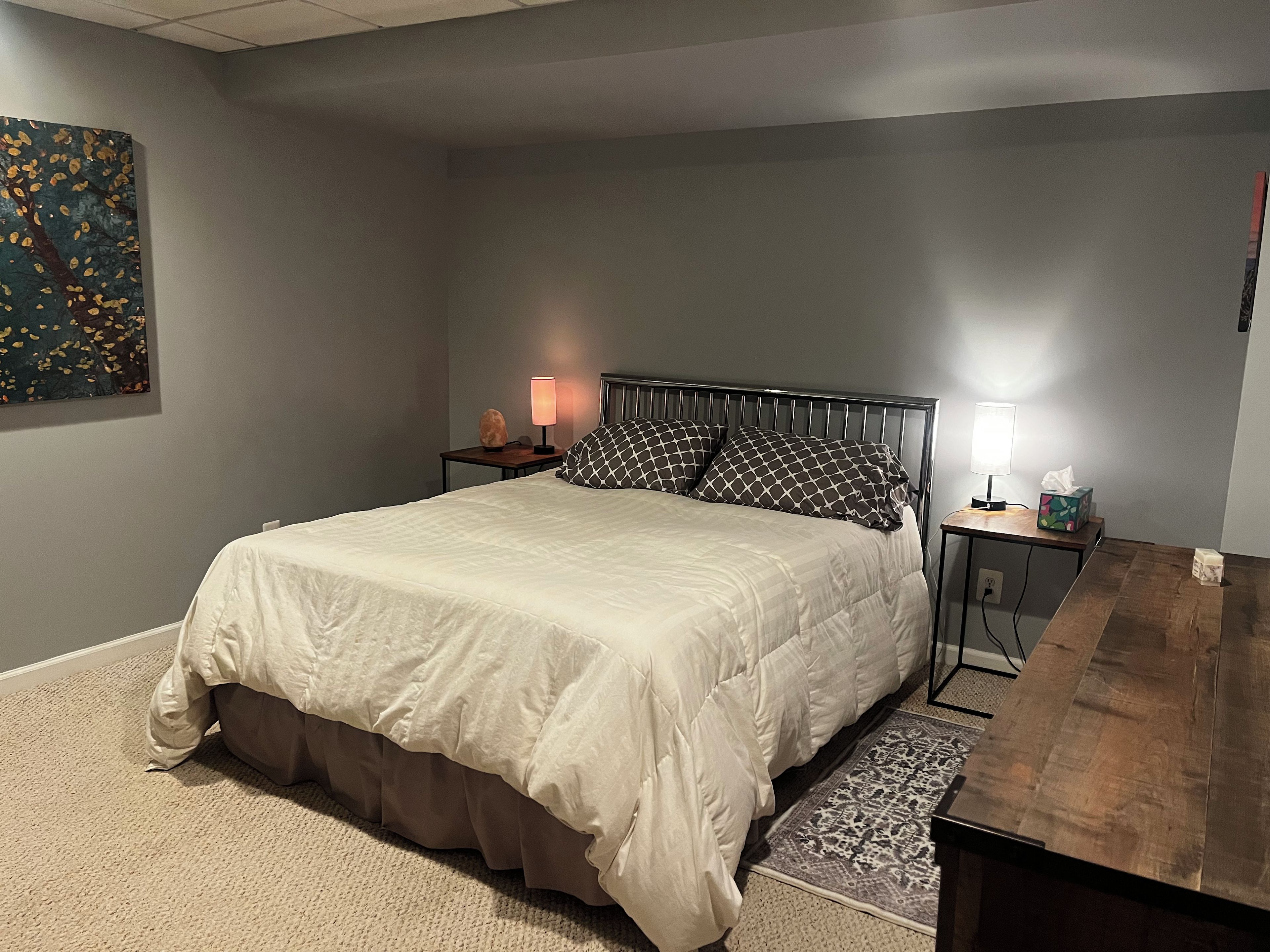 Un dormitorio con una cama, mesitas de noche, una lámpara y un cuadro en la pared.