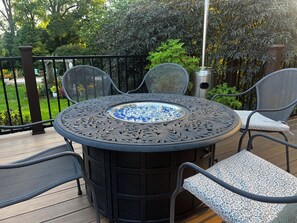 A round outdoor table with a built-in fire feature surrounded by four chairs with cushioned seats.