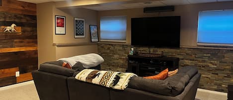 A home theater room with a large sectional sofa, a flat-screen TV, and a stone accent wall.