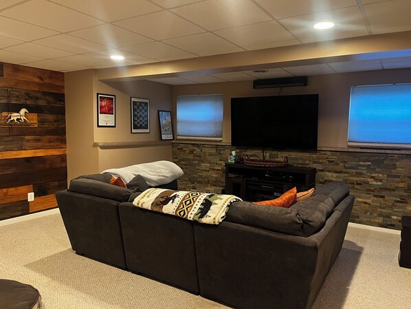 A home theater room with a large sectional sofa, a flat-screen TV, and a stone accent wall.