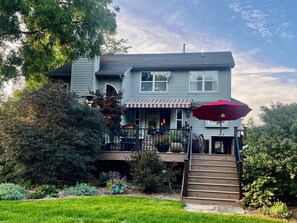 A two-story house with a covered porch, a red umbrella, and a staircase leading to the entrance.