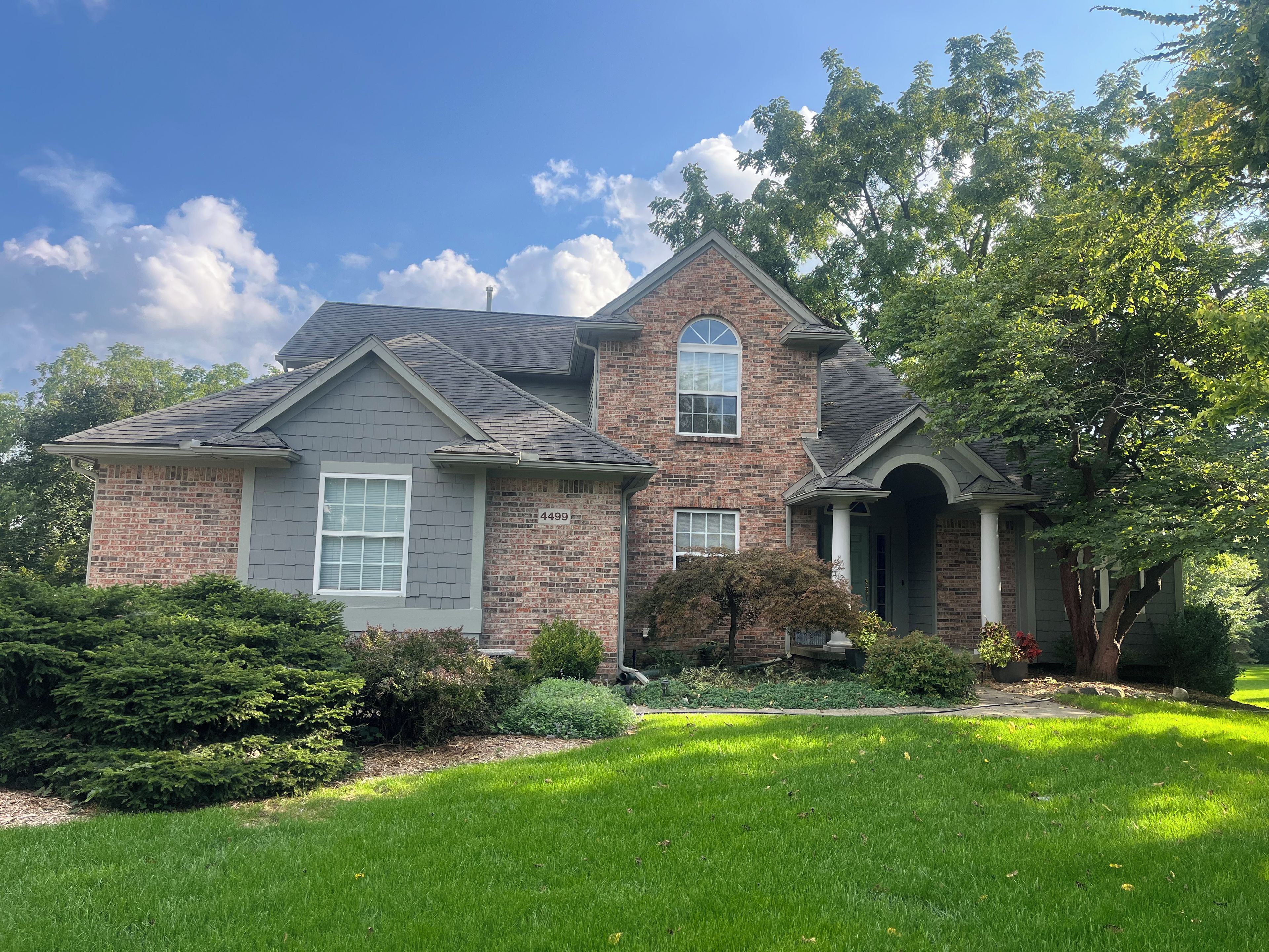 A two-story house with a brick facade, a grey roof, and a well-maintained lawn.