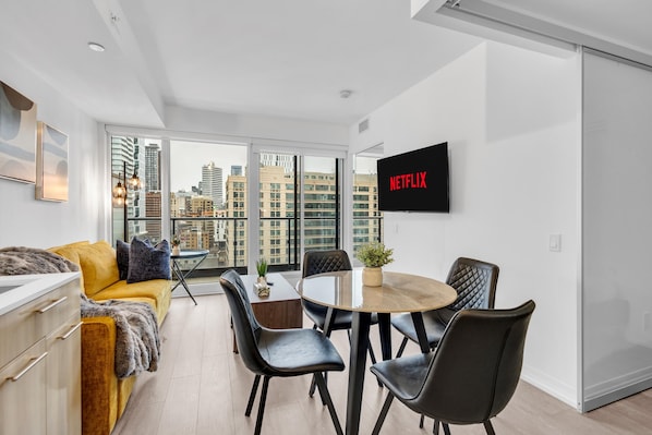 A modern living room with a sofa, dining table, chairs, a TV, and a city view. - Downtown Retreat Near Union Station (Toronto)