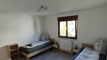 A room with two single beds, a wooden floor, a window with a view, a radiator, and a small table.