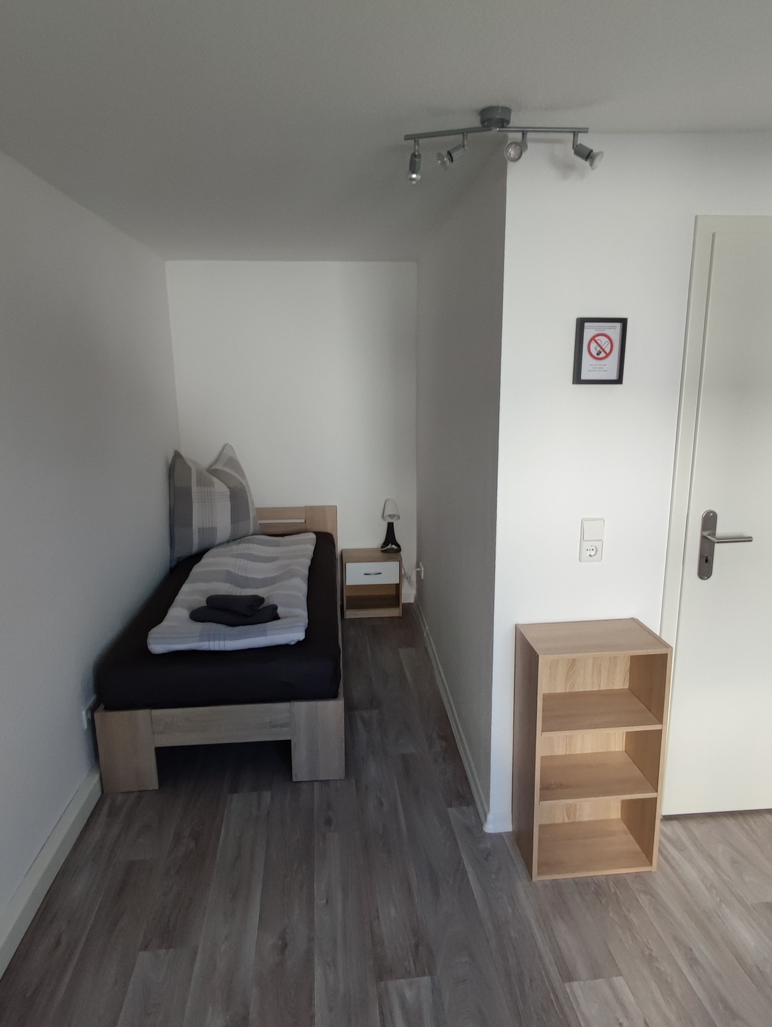 Ein Schlafzimmer mit Bett, Nachttisch, Lampe und einer Tür mit einem Schild.