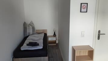 A bedroom with a bed, bedside table, lamp, and a door with a sign.