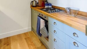 Une cuisine de taille réduite, dotée d’un plan de travail en bois, d’une cuisinière à gaz et de meubles de couleur bleu clair.