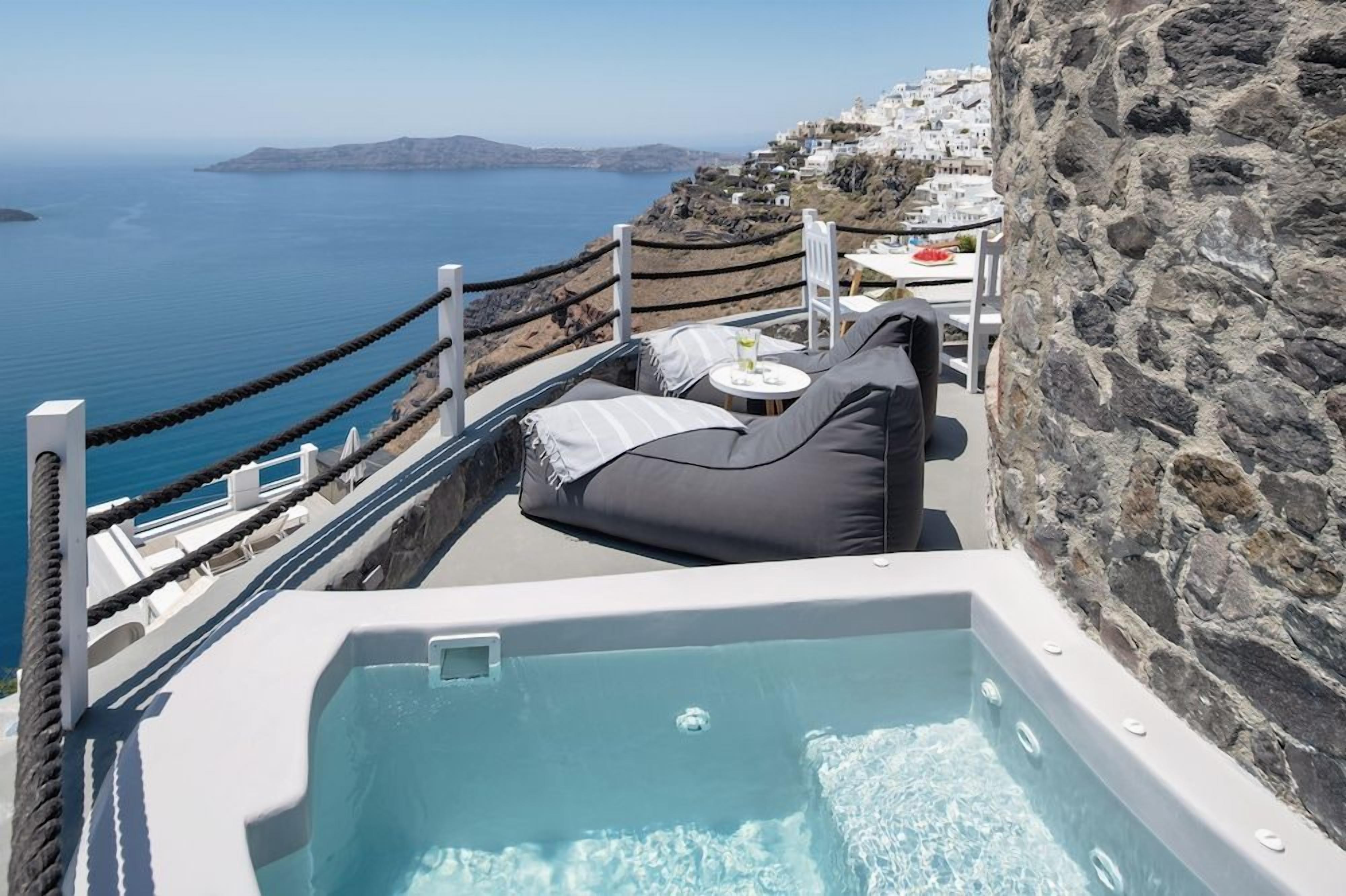 Eine Dachterrasse mit Whirlpool, Sitzgelegenheit und Blick auf das Meer und weiße Gebäude.