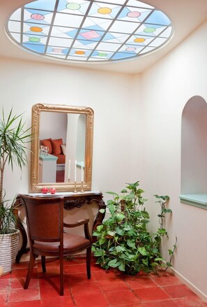 Una habitación con una silla de madera, un espejo, una planta en maceta y un ventanal con vistas.