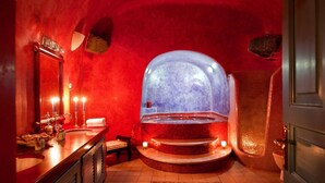 Ein Badezimmer mit roten Wänden, einer großen, runden Badewanne, einem Waschtisch mit Spiegel und einer Duschkabine.