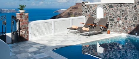 Área de piscina com espreguiçadeiras e vista para o mar.
